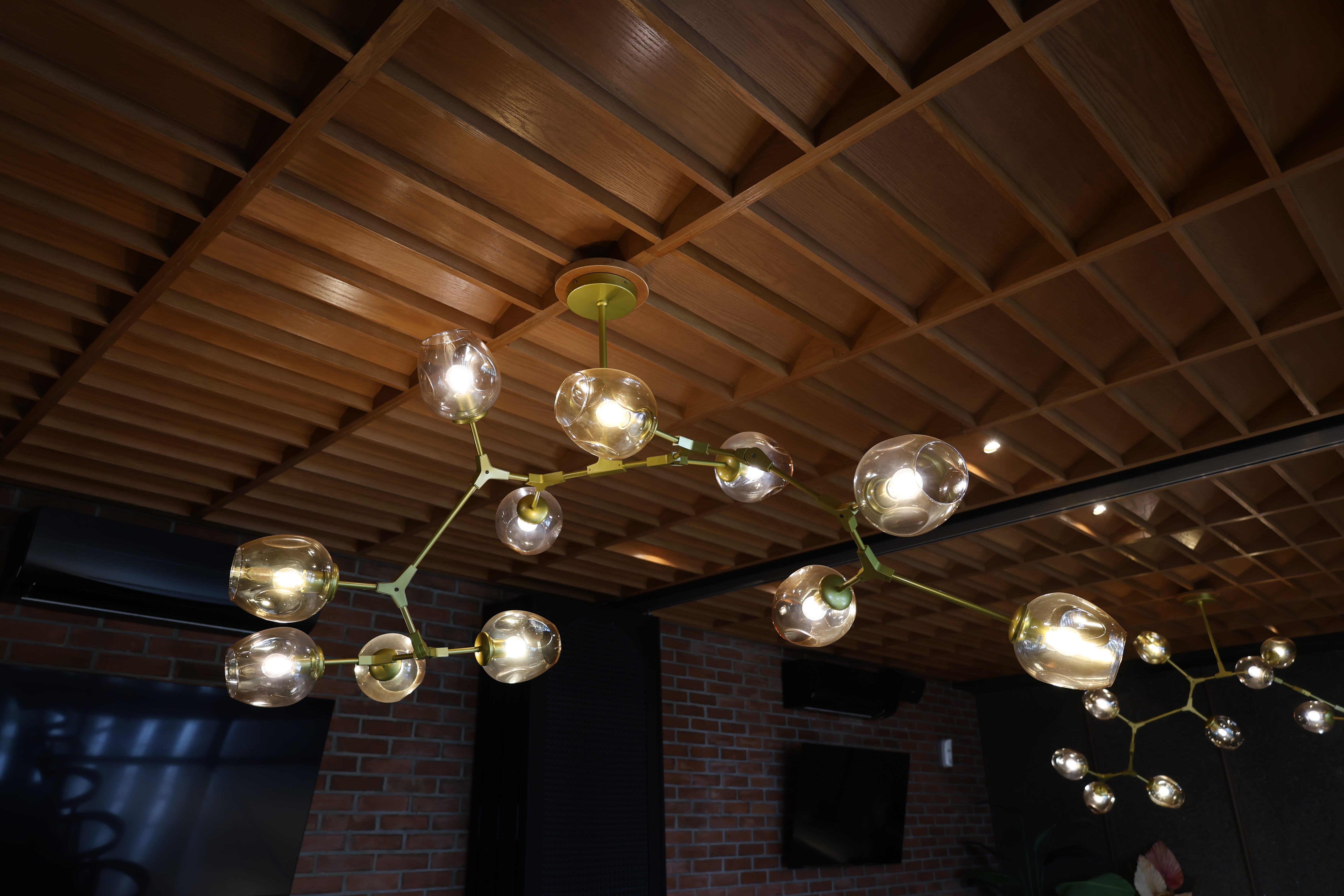 Looking up at solid wood grid lattice ceiling with brass chandeliers at BSteak Kelapa Gading by Reywood